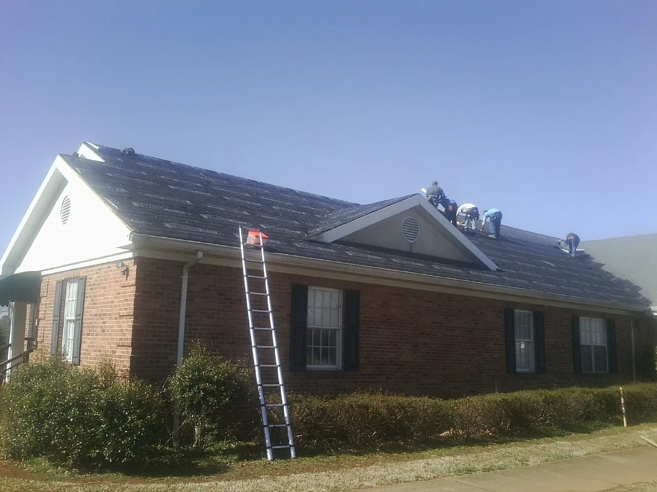 Crew tearing shingles off a brick ranch roof with a ladder set — Metal Roof Repair work by our crew in Airway Heights