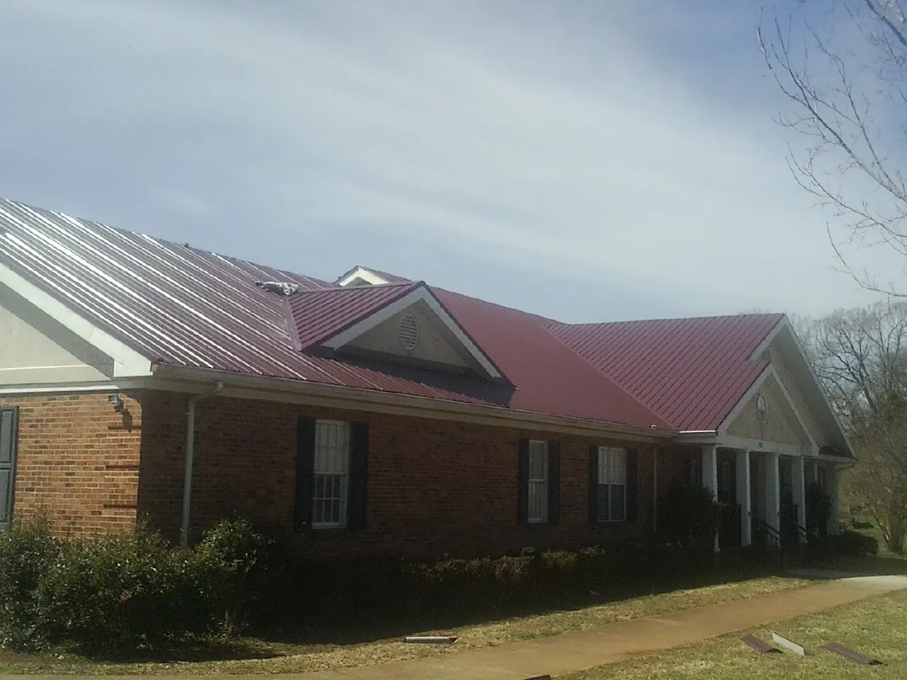 Red metal roof with gabled entries on a long brick building, from a Hail Damage Roof Repair job in Airway Heights