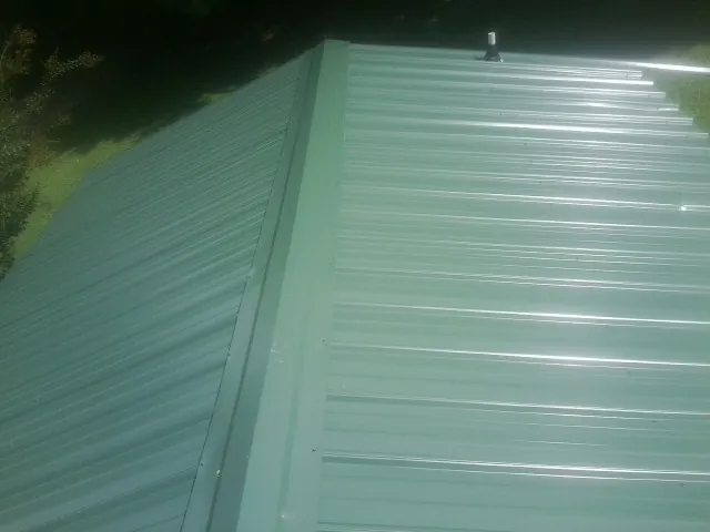 New green metal panels meeting at the ridge of a roof — Flat Roof Repair work by our crew in Airway Heights