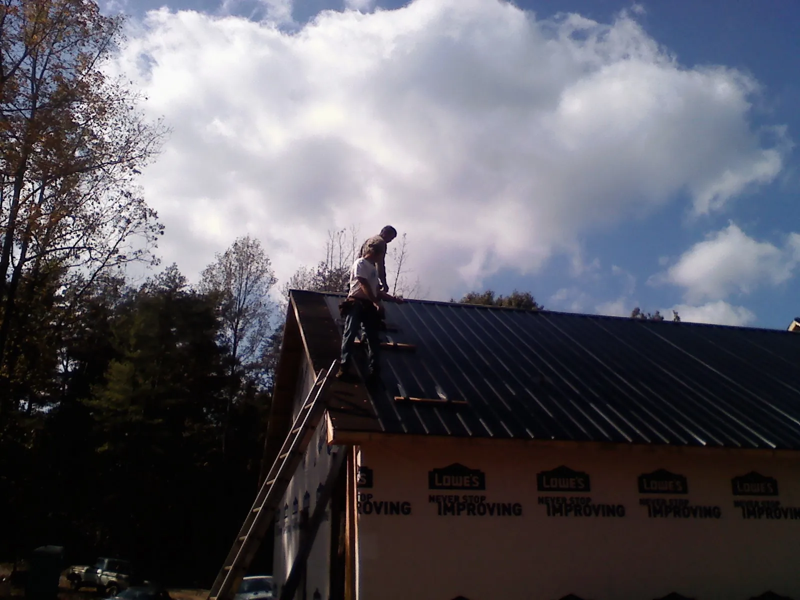Roofer fastening dark metal panels high against a cloudy sky, from a Roof Inspection job in Airway Heights