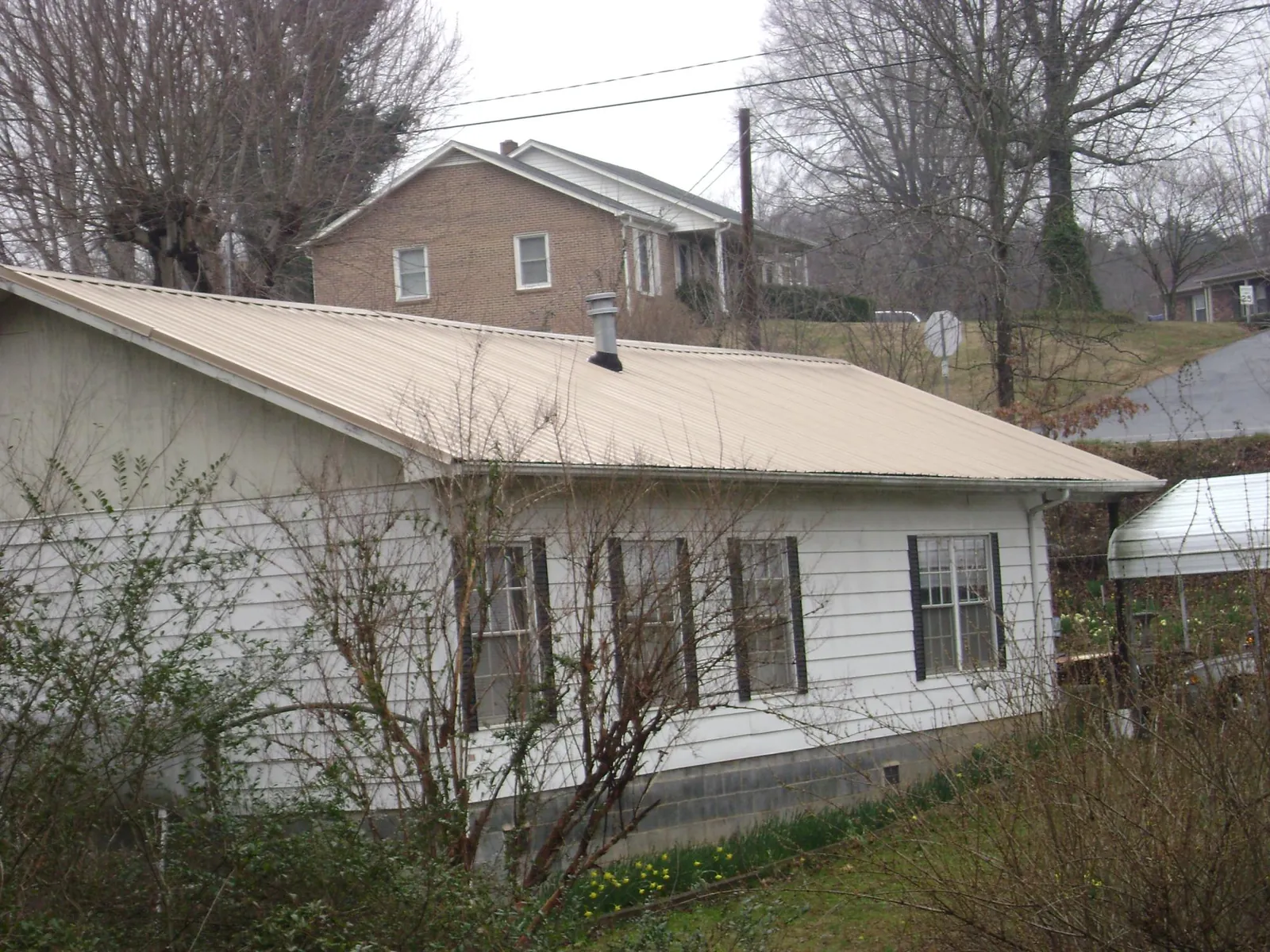 Tan metal roof on a white sided house set into a hillside — Commercial Roofing by Roofing Brothers in Airway Heights